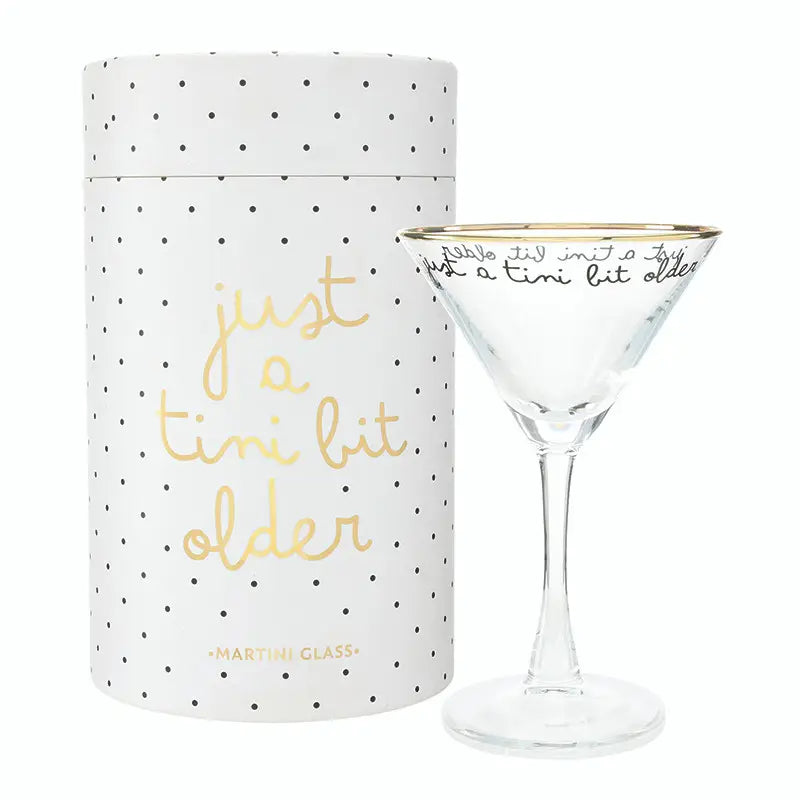 Just a Tini Bit Older gold rim martini glass with black script and just a tini bit older cursive text beside white polka dot gift tube with gold foil Just a Tini Bit Older script on white background – Bliss by Cori
