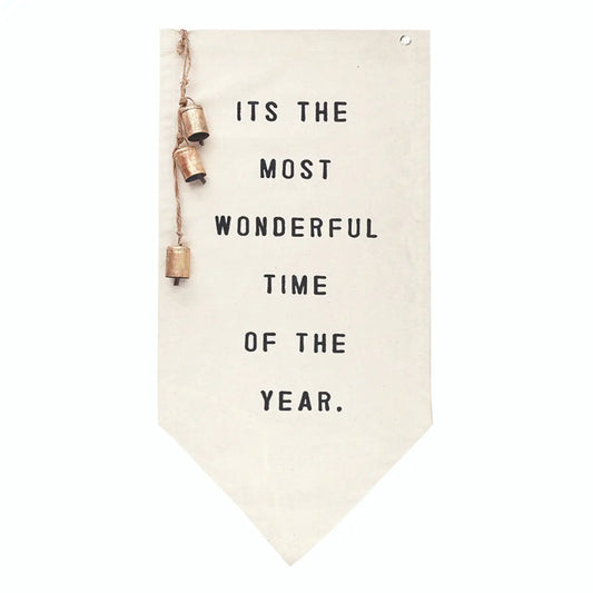Cream canvas pennant wall banner with black block text reading Its the Most Wonderful Time of the Year and three antique gold bells on jute cord on white background – Bliss by Cori
