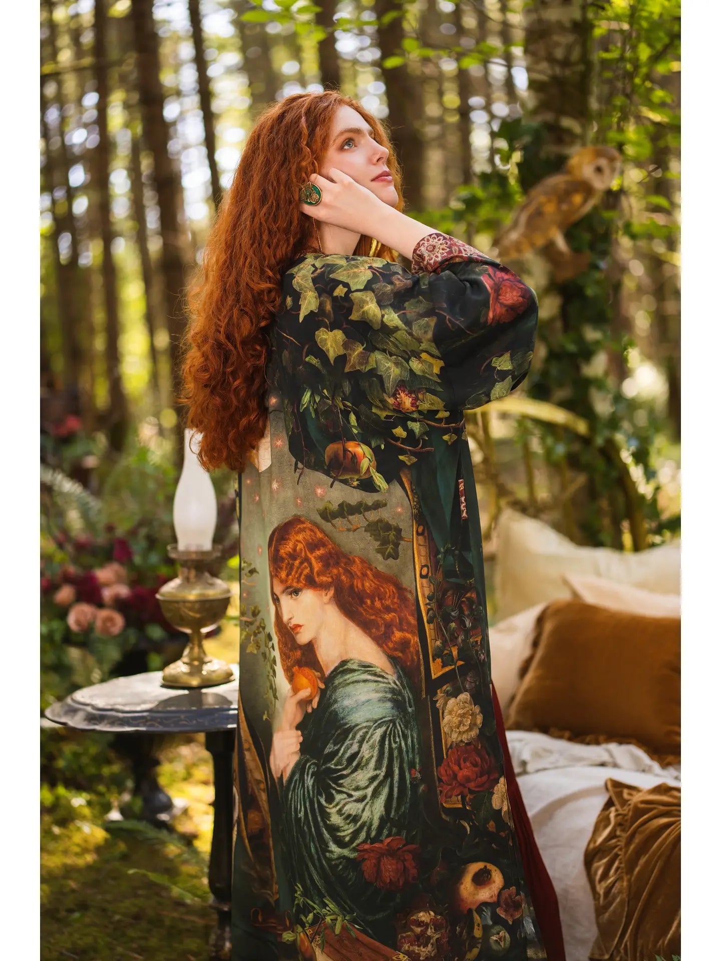 Side profile of red-haired model in forest glade wearing Solstice Opera Duster Kimono, Rossetti Proserpine portrait visible on back, barn owl perched on branch, oil lamp on table — Bliss by Cori