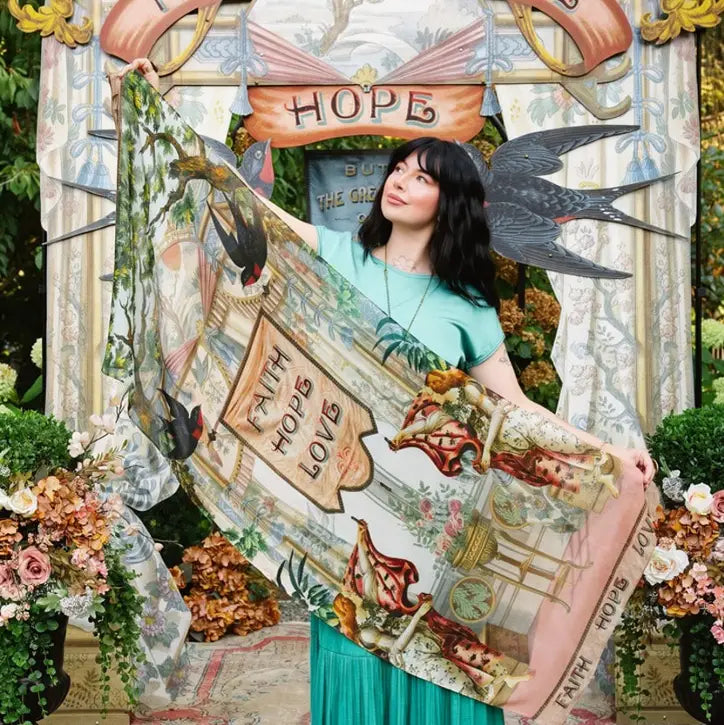 Model holding Book of Love scarf open diagonally, showing Faith Hope Love banner, swallows, and vintage artwork | Bliss by Cori
