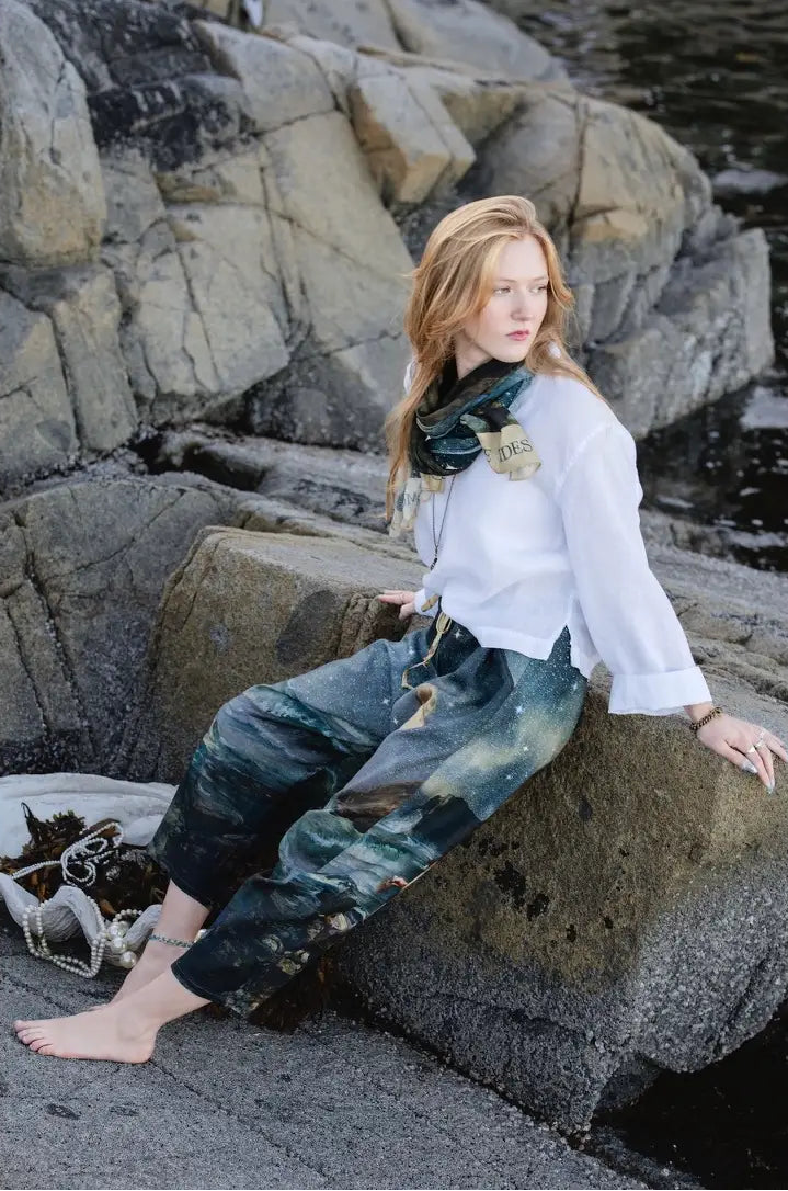 Model seated on shoreline rocks in the Siren cropped Artist Pants | Bliss by Cori