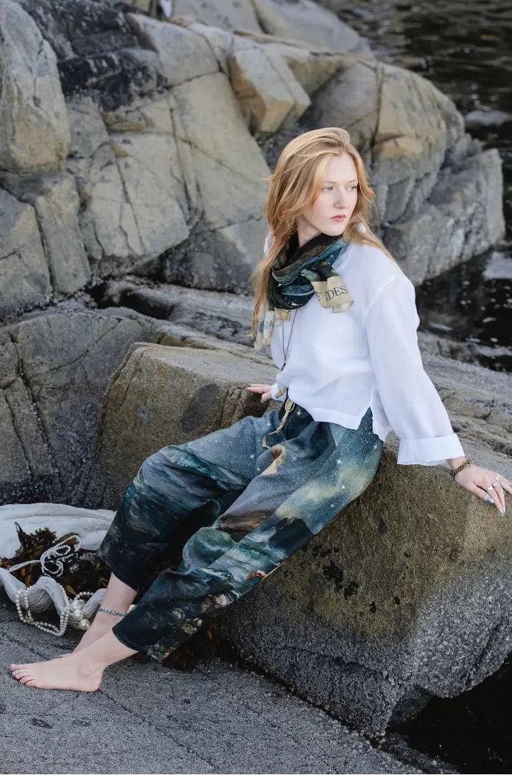 Seated model wearing the Siren cropped mermaid pants among coastal rocks | Bliss by Cori