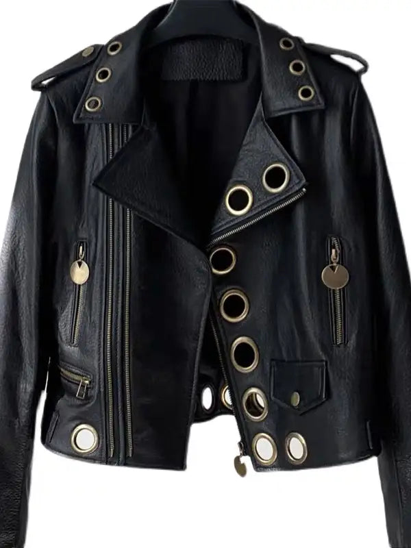 Flat lay front detail of black lambskin leather moto jacket showing asymmetrical lapel collar, oversized hollow metal ring embellishments, dual zipper pockets, and gold coin hardware on white background — Bliss by Cori