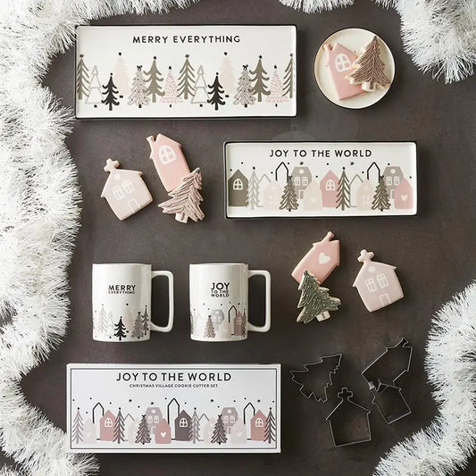 Overhead flat lay of Christmas Village Collection featuring Merry Everything ceramic tray, Joy to the World tray, mugs, cookie cutters and holiday cookies styled with white garland – Bliss by Cori
