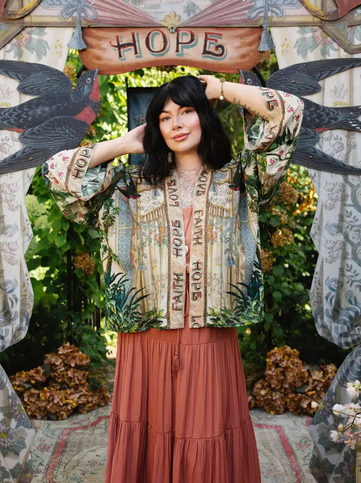 Model wearing Book of Love cropped kimono over a coral dress with hands raised, showing wide floral sleeves | Bliss by Cori