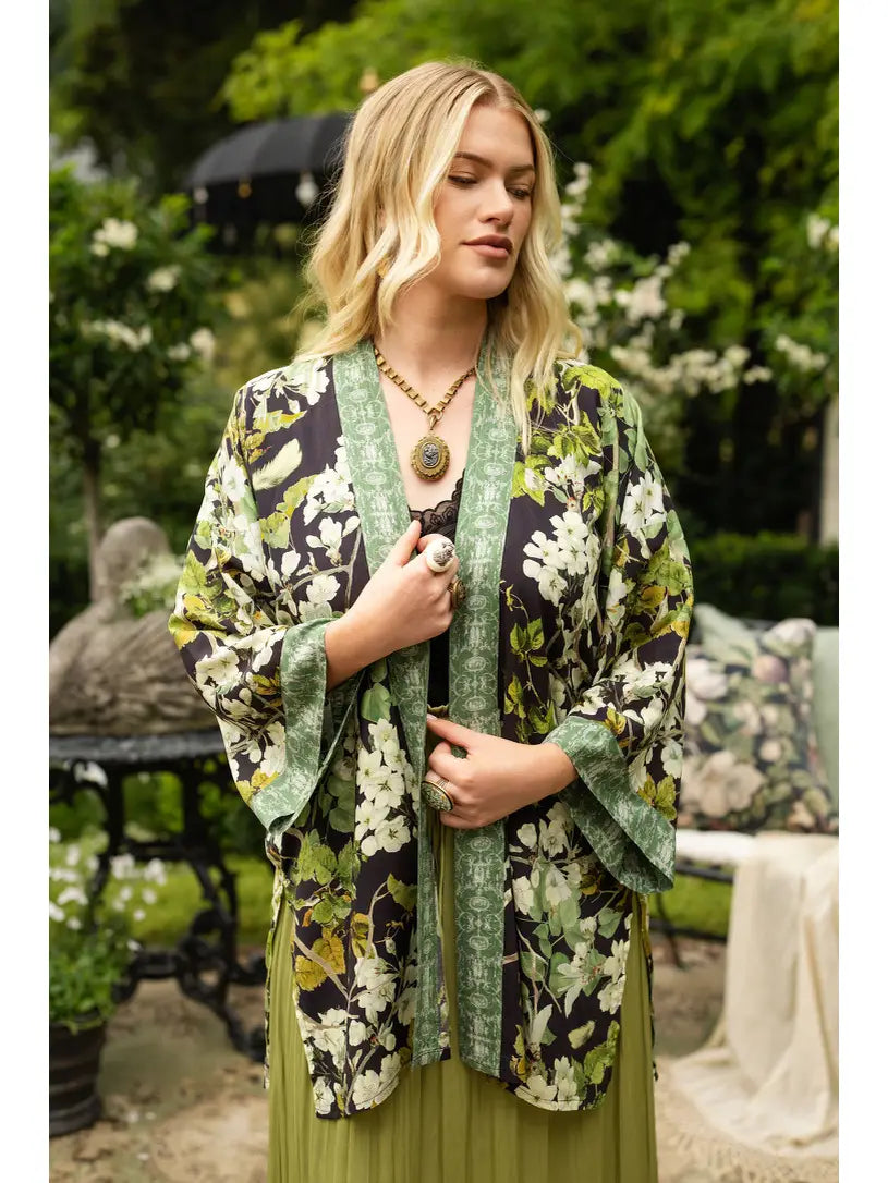 Front view of the Equinox duster layered over a sage green dress beside white siding and flowers | Bliss by Cori