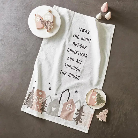 White cotton Twas the Night Before Christmas tea towel styled on a gray surface with pink ornaments, embroidered Christmas tree cookie cutters and ceramic holiday accessories – Bliss by Cori
