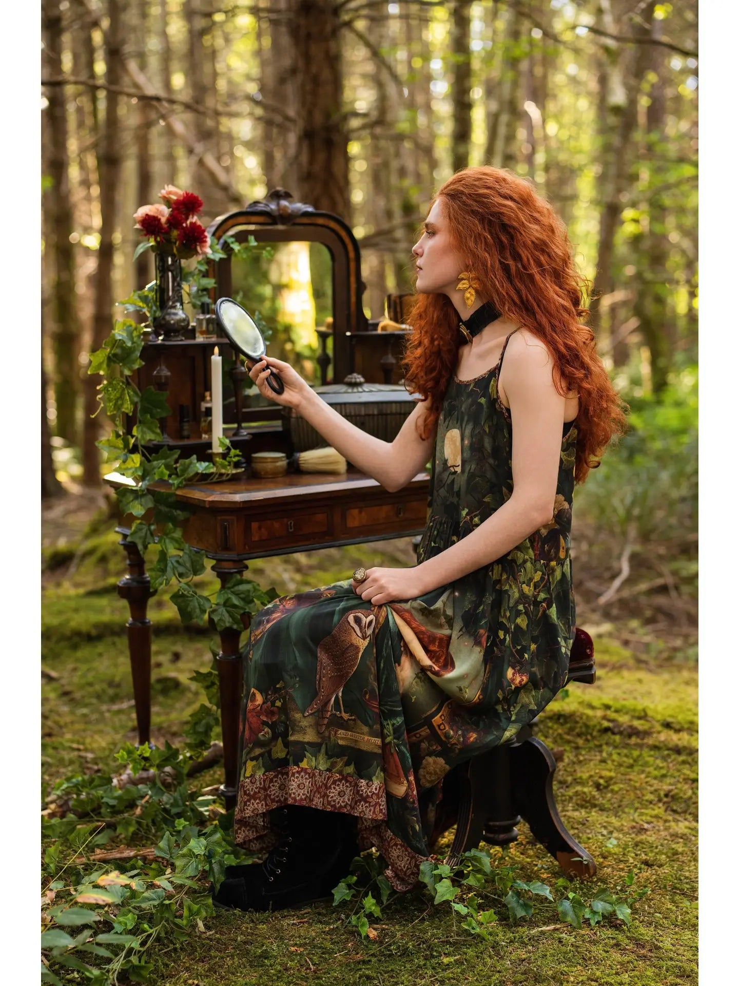 Full-length front view of red-haired model in mossy forest wearing Solstice Bohéme Maxi Slip Dress, Rossetti Proserpine and moon print visible, enchanted outdoor bedroom with antique brass bed behind — Bliss by Cori