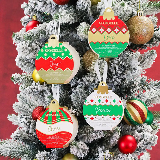 Spongellé Joy Snowberry body buffer ornament in red and green holiday packaging hanging on a flocked Christmas tree — Bliss by Cori Boutique