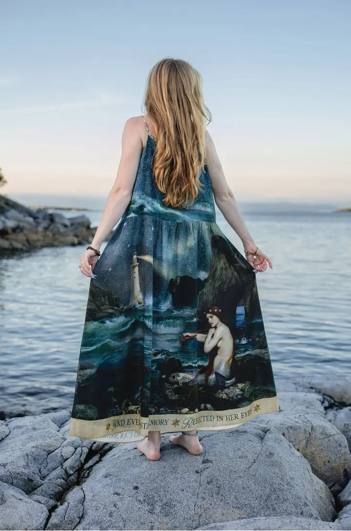 Model seated among coastal rocks in the flowing Siren celestial maxi slip dress | Bliss by Cori