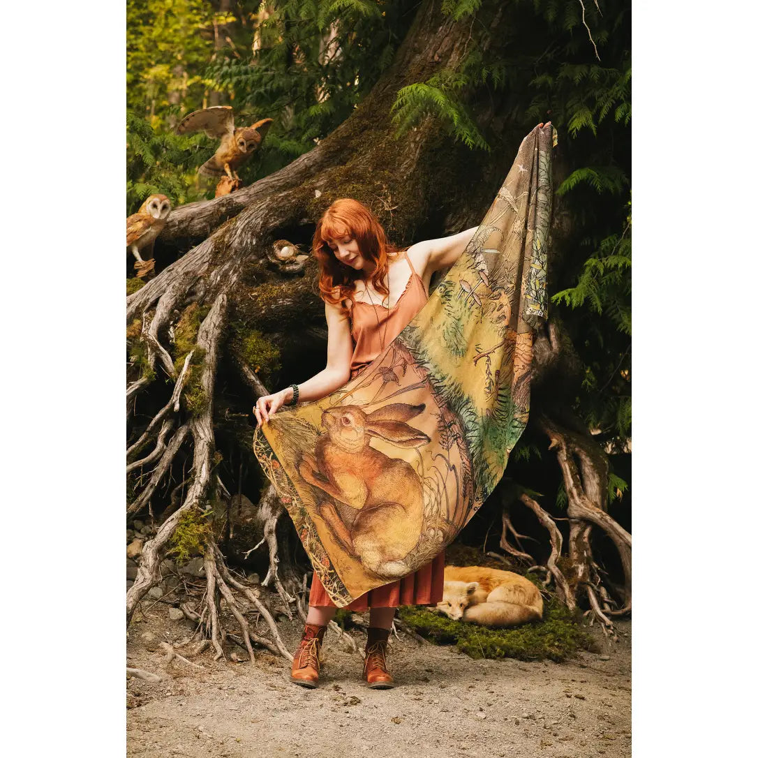 Model draped in Woodland Wisdom Bohemian Scarf worn as a wrap, full rabbit print centrepiece and green woodland border visible, moss-covered tree roots and owls in background — Bliss by Cori