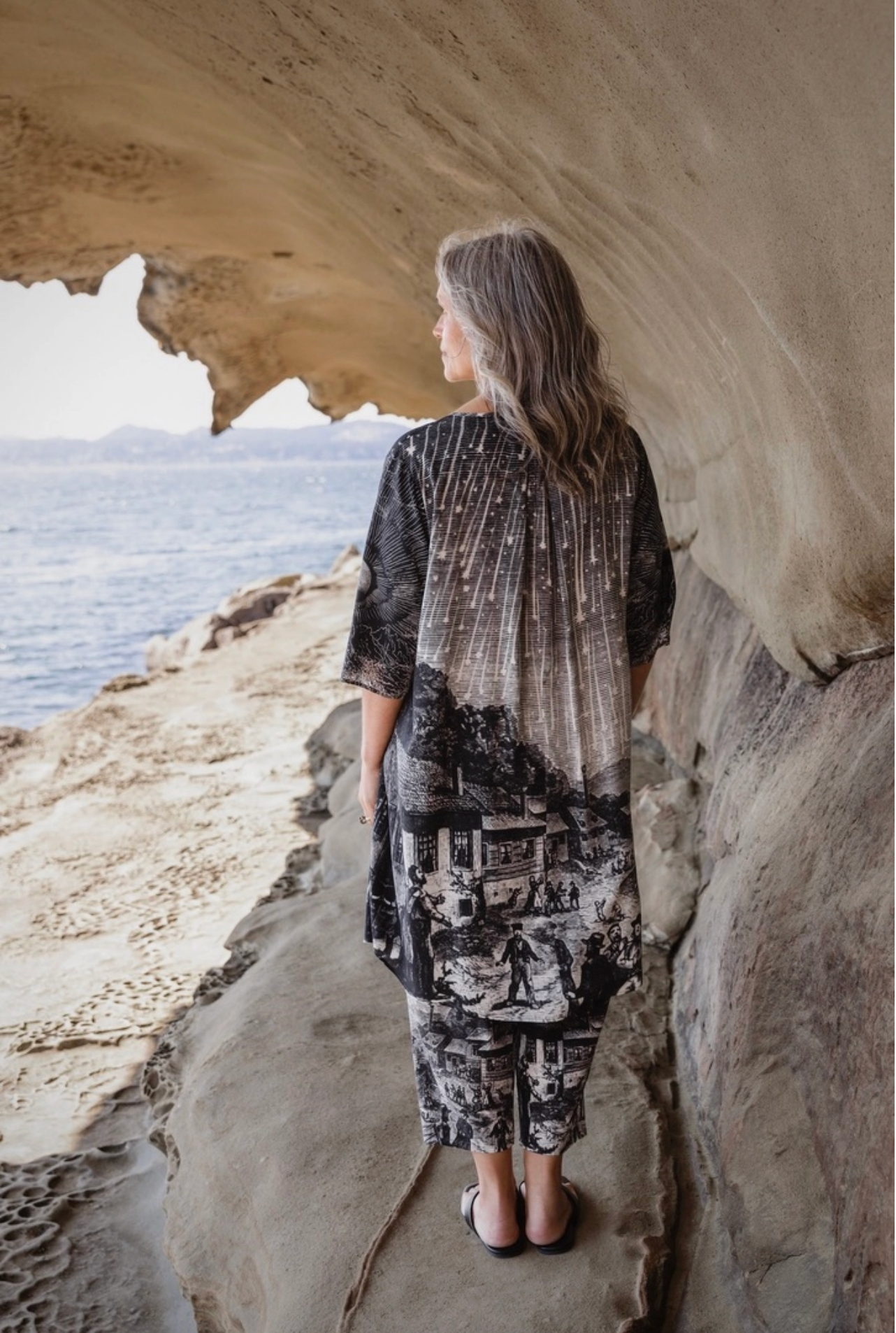 Back view of Stargazer Artist Dress showing full Leonid meteor shower engraving print on skirt, worn on rocky coastal cliffs | Bliss by Cori Boutique