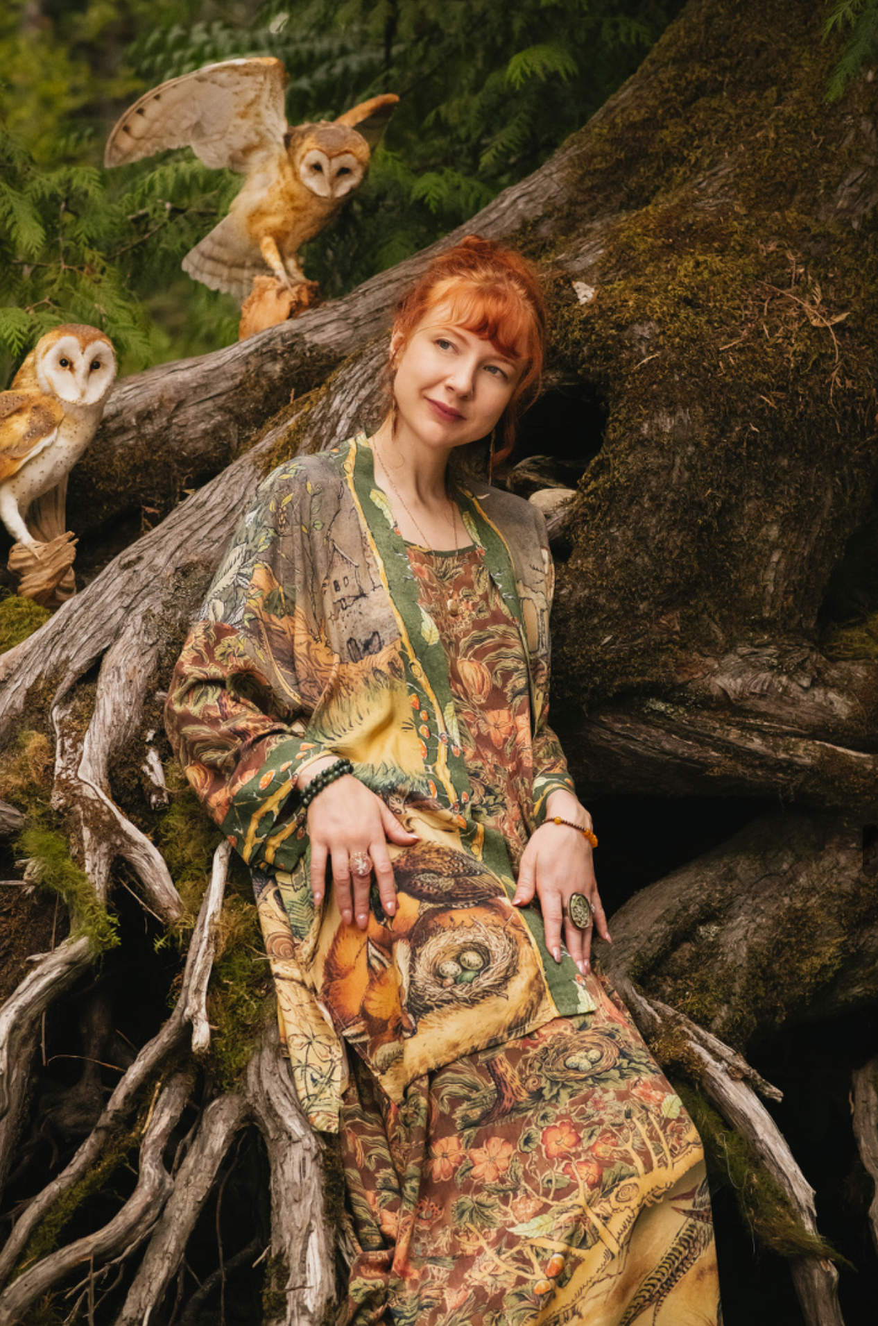 Woodland Wisdom Matinée Duster Kimono front view, model seated among ancient mossy tree roots with two barn owls perched nearby, showing fox and pheasant nest print — Bliss by Cori
