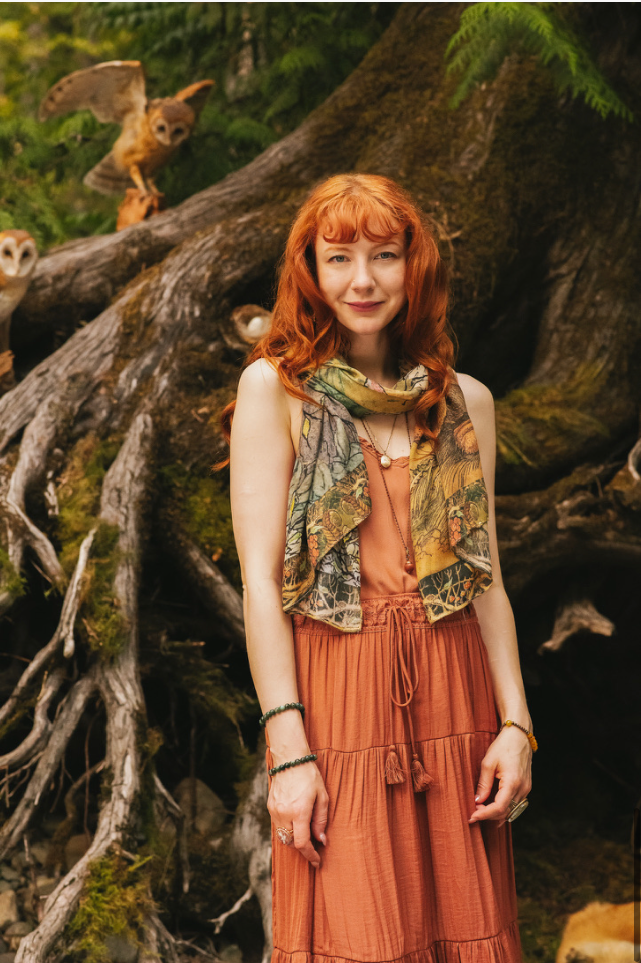 Model wearing Woodland Wisdom Bohemian Scarf draped over shoulders as a shawl, styled with rust tiered skirt and lace-up boots before ancient mossy tree roots, owls perched nearby — Bliss by Cori
