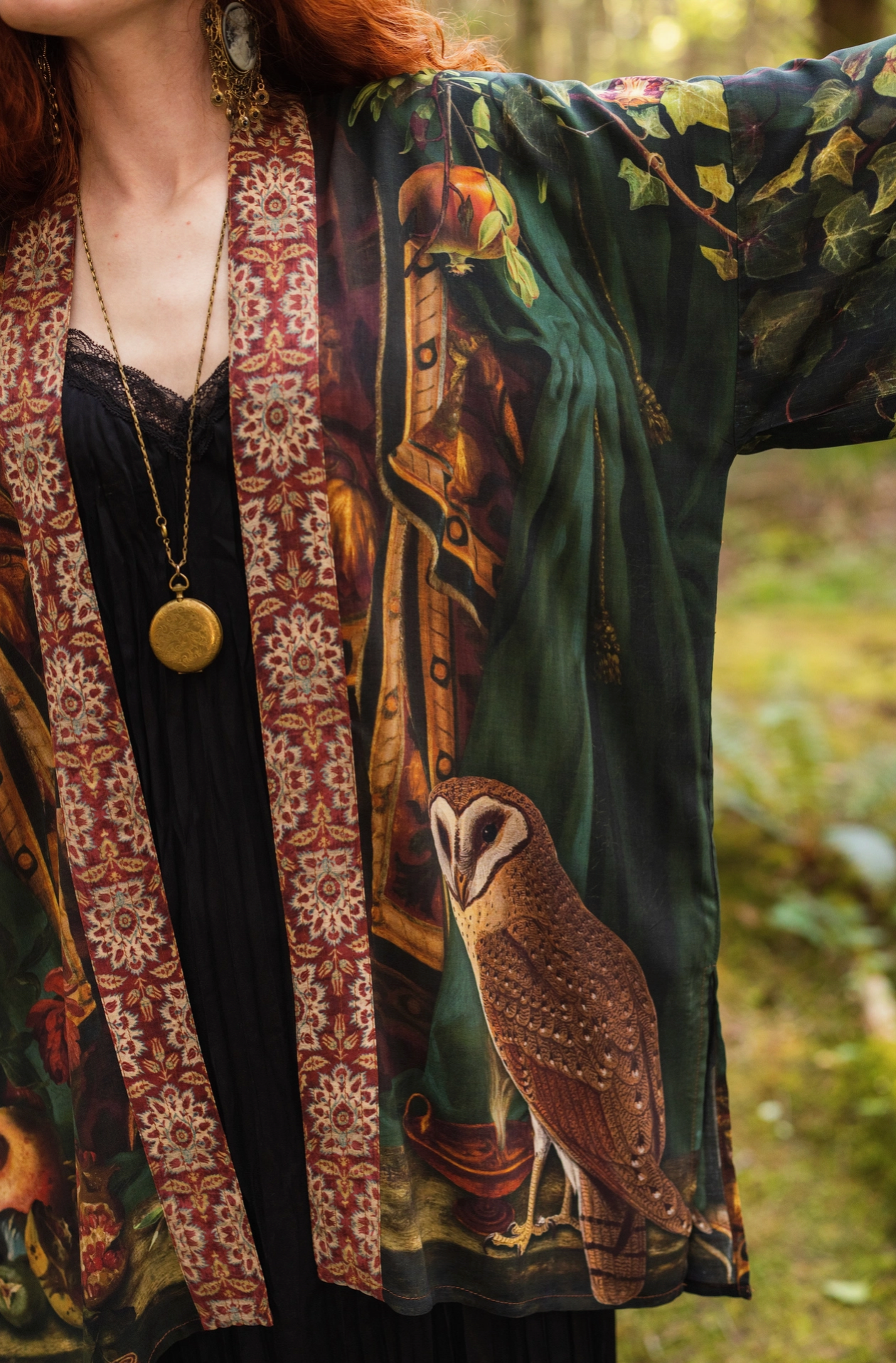 Close-up of red-haired model wearing Solstice Matinée Mid-Length Duster Kimono open over black lace cami, barn owl print visible on front panel, tapestry border trim and gold locket necklace — Bliss by Cori