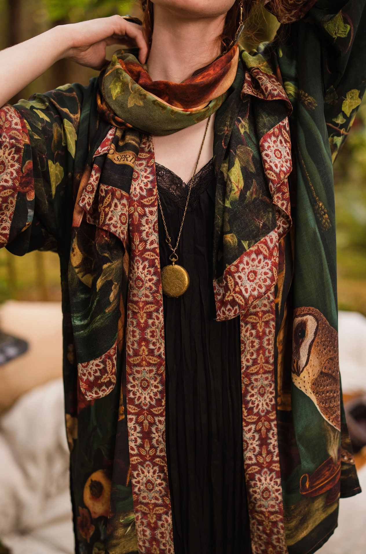 Close-up of red-haired model styling Solstice Bohemian Scarf as a neck wrap over Solstice Kimono, showing tapestry border and barn owl print with gold locket necklace layered over black lace cami — Bliss by Cori