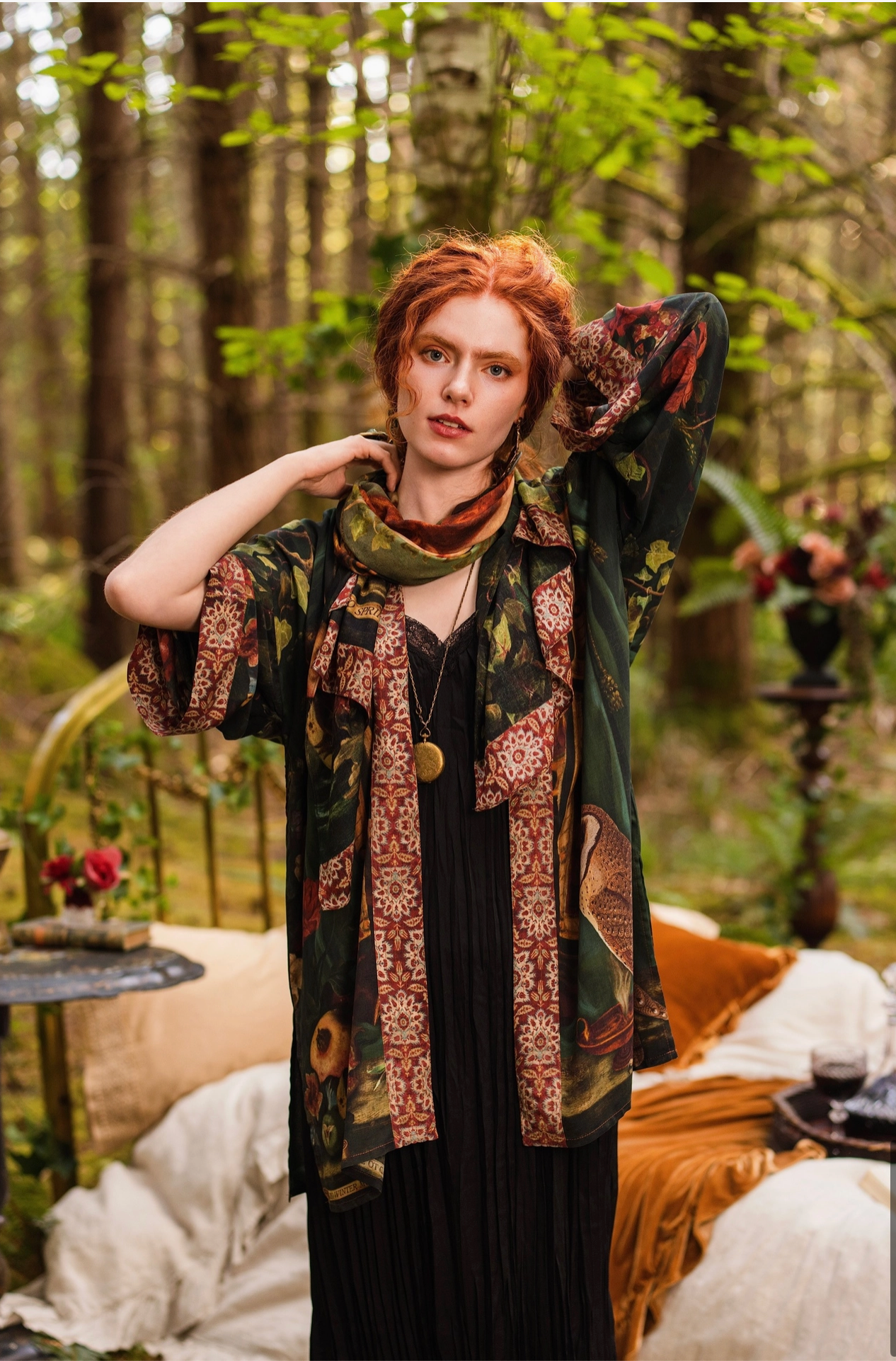 Red-haired model in enchanted forest bedroom styling Solstice Bohemian Scarf as a neck wrap over Solstice Kimono and black dress, terracotta tapestry border and barn owl print visible, gold locket necklace, velvet cushions behind — Bliss by Cori