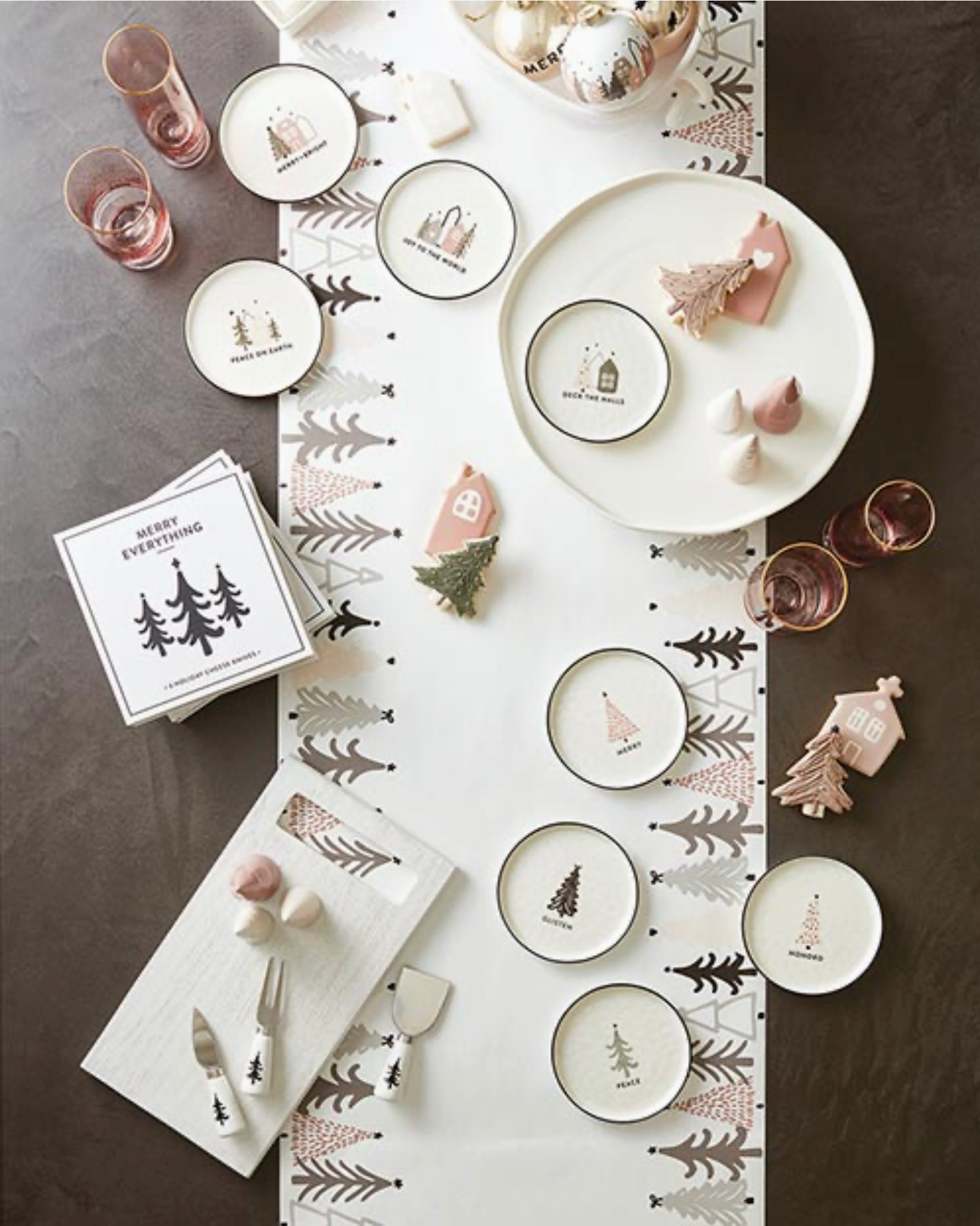 Overhead flat lay of Christmas Village Collection holiday appetizer plates styled on a festive table runner with rose gold glasses, pink ceramic house ornaments and holiday napkins – Bliss by Cori
