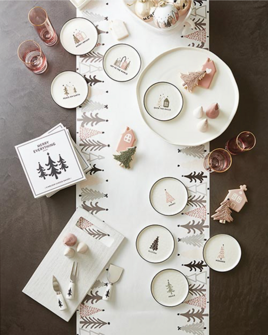 Overhead flat lay of Christmas Village Collection holiday appetizer plates styled on a festive table runner with rose gold glasses, pink ceramic house ornaments and holiday napkins – Bliss by Cori
