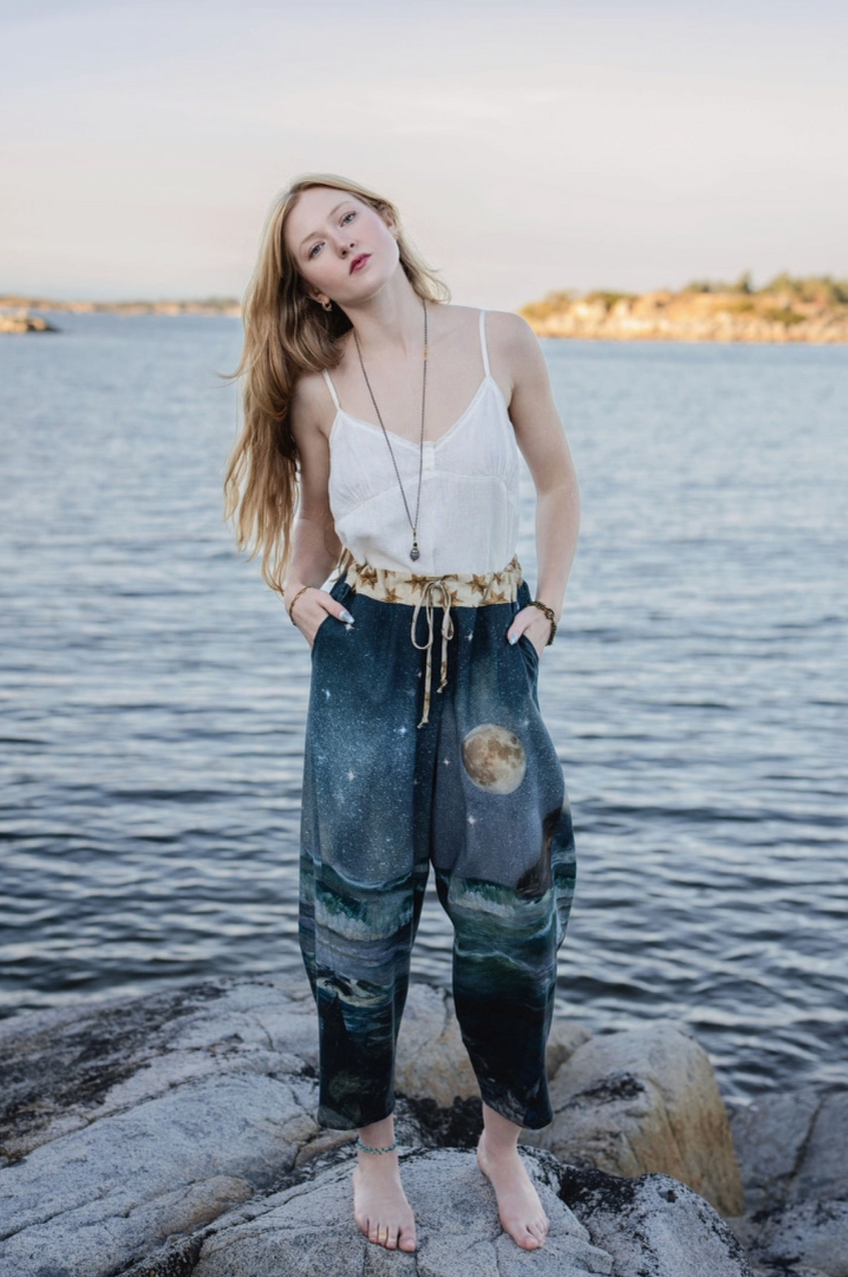 Model standing on shoreline rocks in the full-print Siren cropped Artist Pants | Bliss by Cori