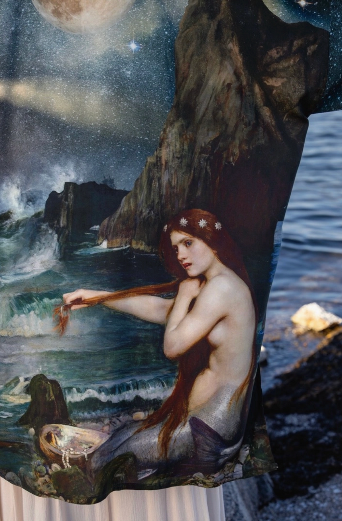 A draped fabric or tapestry featuring a fantasy seascape painting with a seated mermaid, rocky coastline, ocean waves, and a starry night sky with a moon | Bliss by Cori