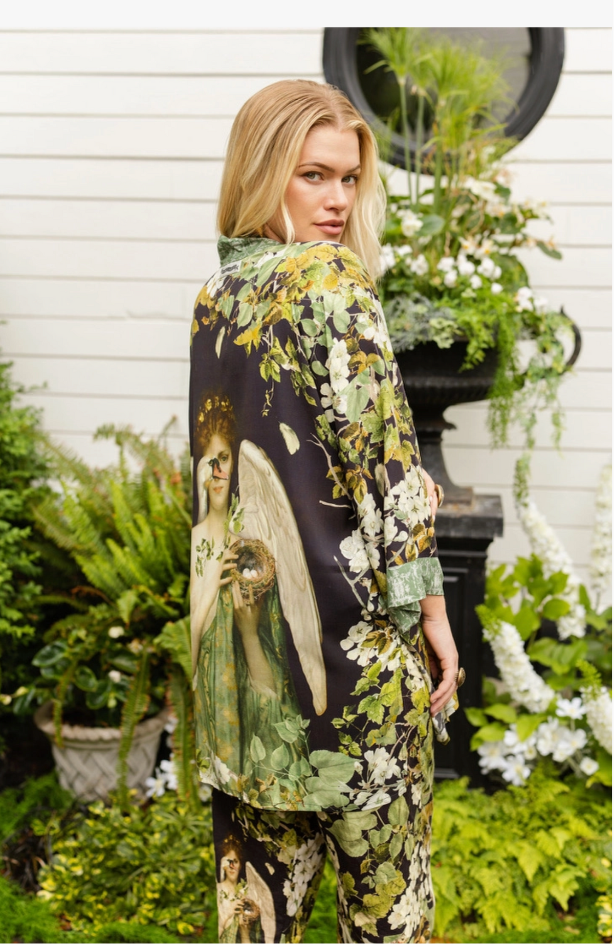 Side view of the Equinox duster layered over a sage green dress beside white siding and flowers | Bliss by Cori