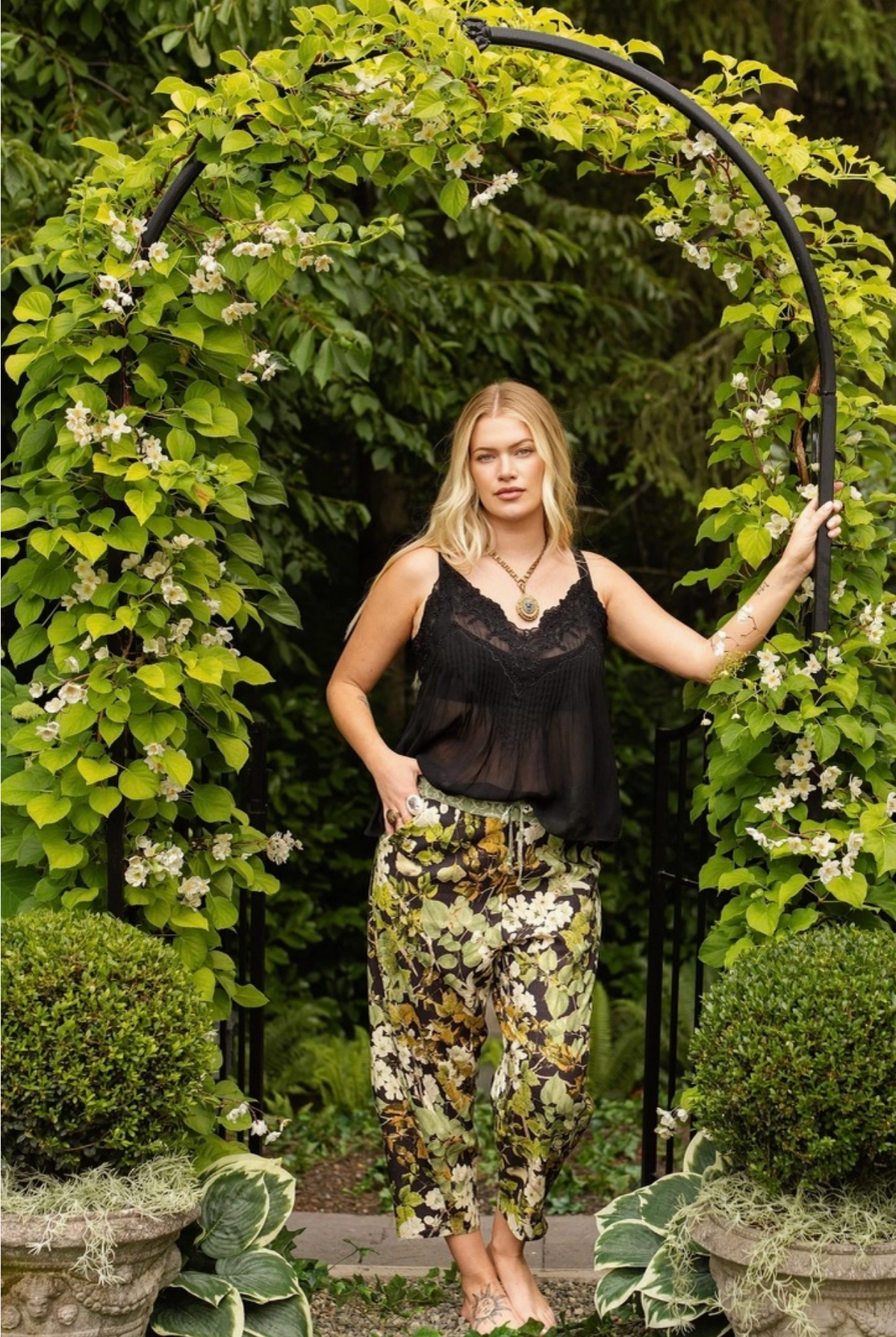 Model wearing the Equinox botanical Artist Pants beneath a leafy garden arch | Bliss by Cori