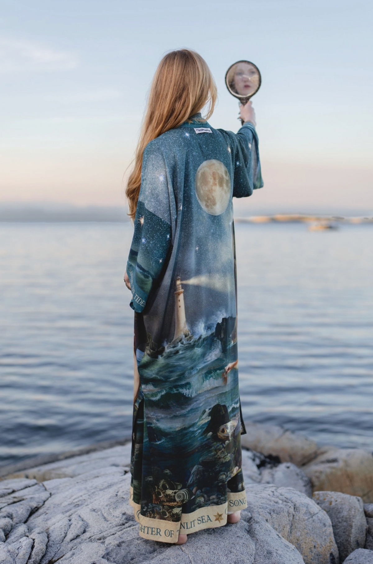 Side view of the long Siren duster flowing beside calm coastal water | Bliss by Cori