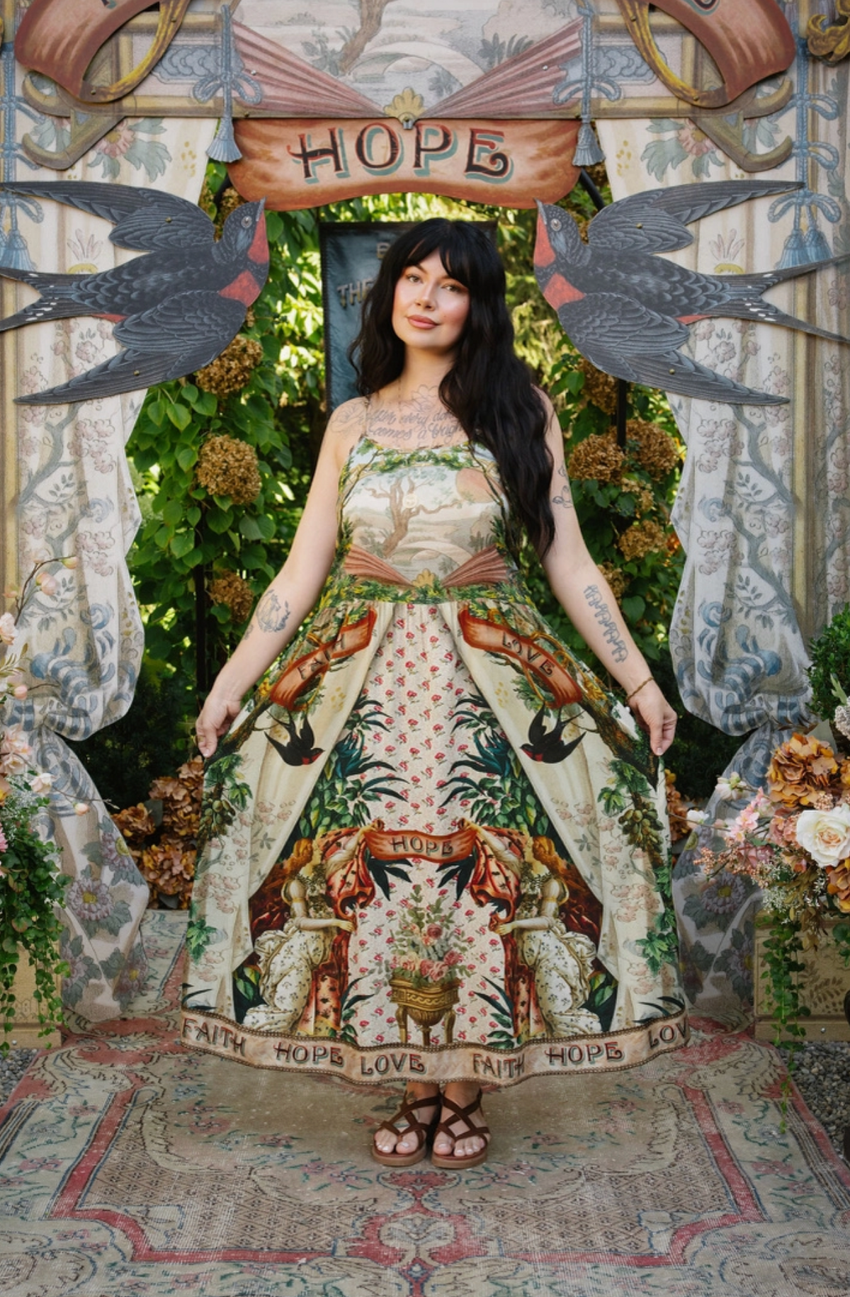 Model holding out the Book of Love maxi dress skirt, showing its scenic bodice and illustrated hem | Bliss by Cori