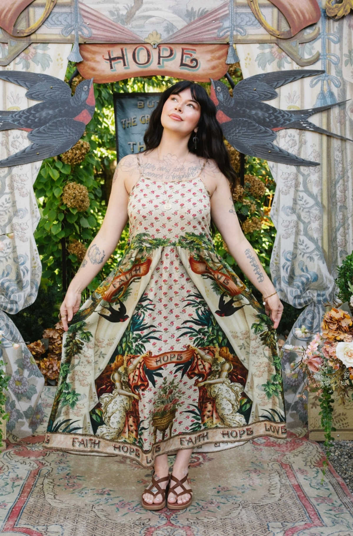 Model holding out the skirt of the Book of Love maxi slip dress, showing its floral bodice and illustrated hem | Bliss by Cori
