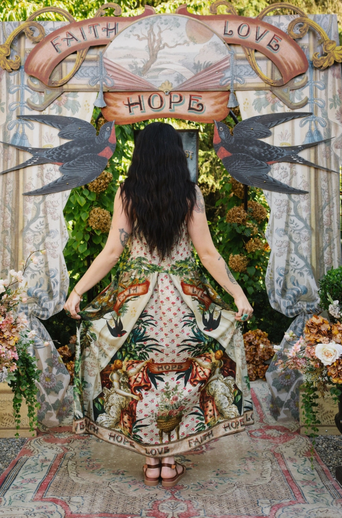 Model holding out the back of the Book of Love dress, showing floral panels, swallows, and lettered hem | Bliss by Cori