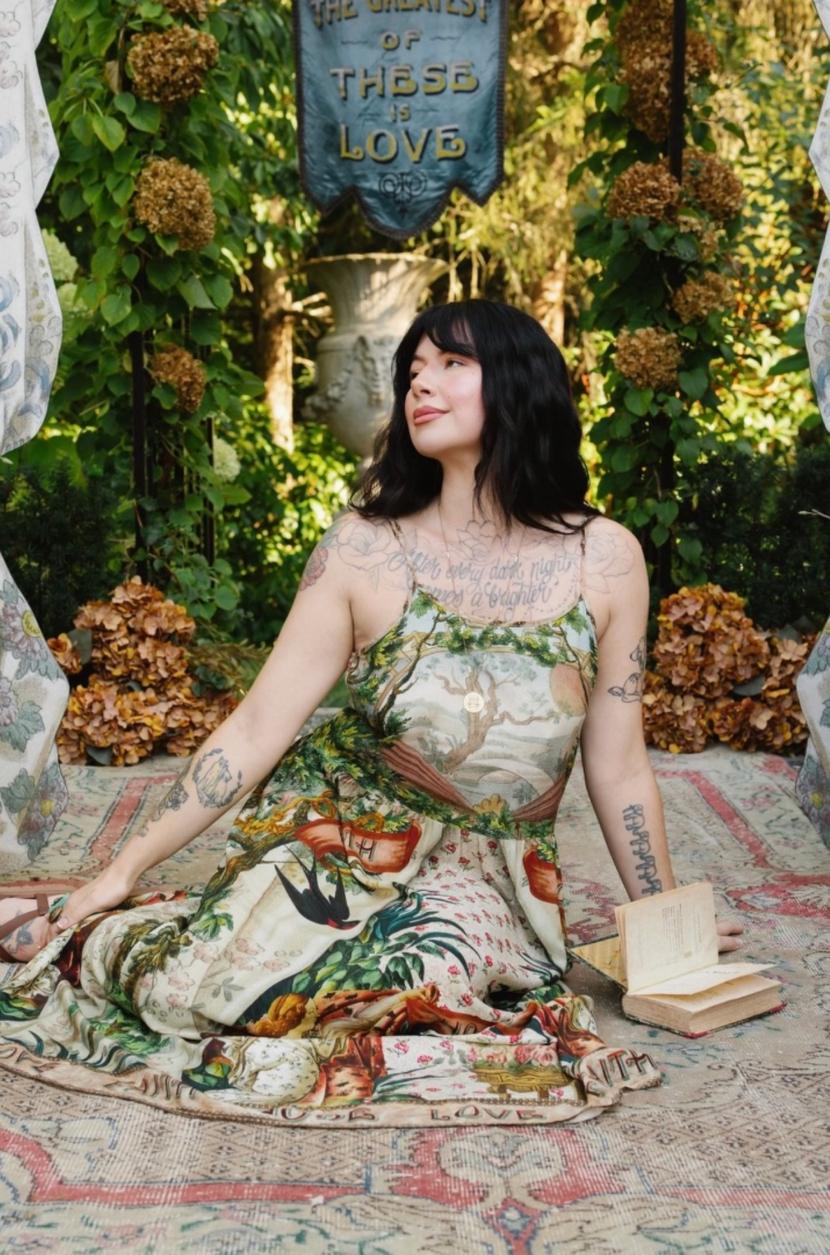 Model seated beside an open book in the Book of Love dress, showing scenic bodice and illustrated skirt | Bliss by Cori
