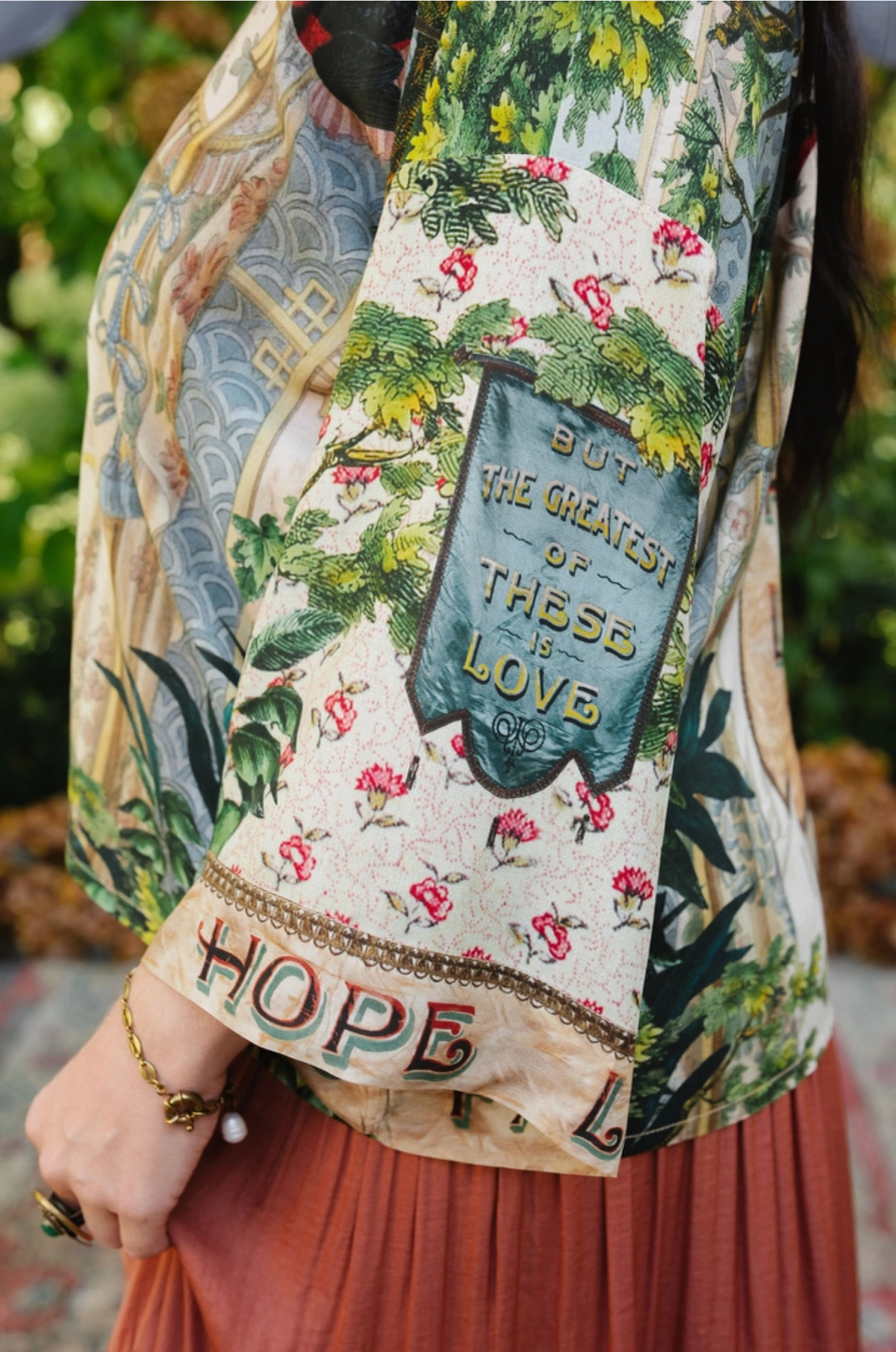 Book of Love kimono sleeve detail with pink flowers and a blue banner reading But the greatest of these is love | Bliss by Cori