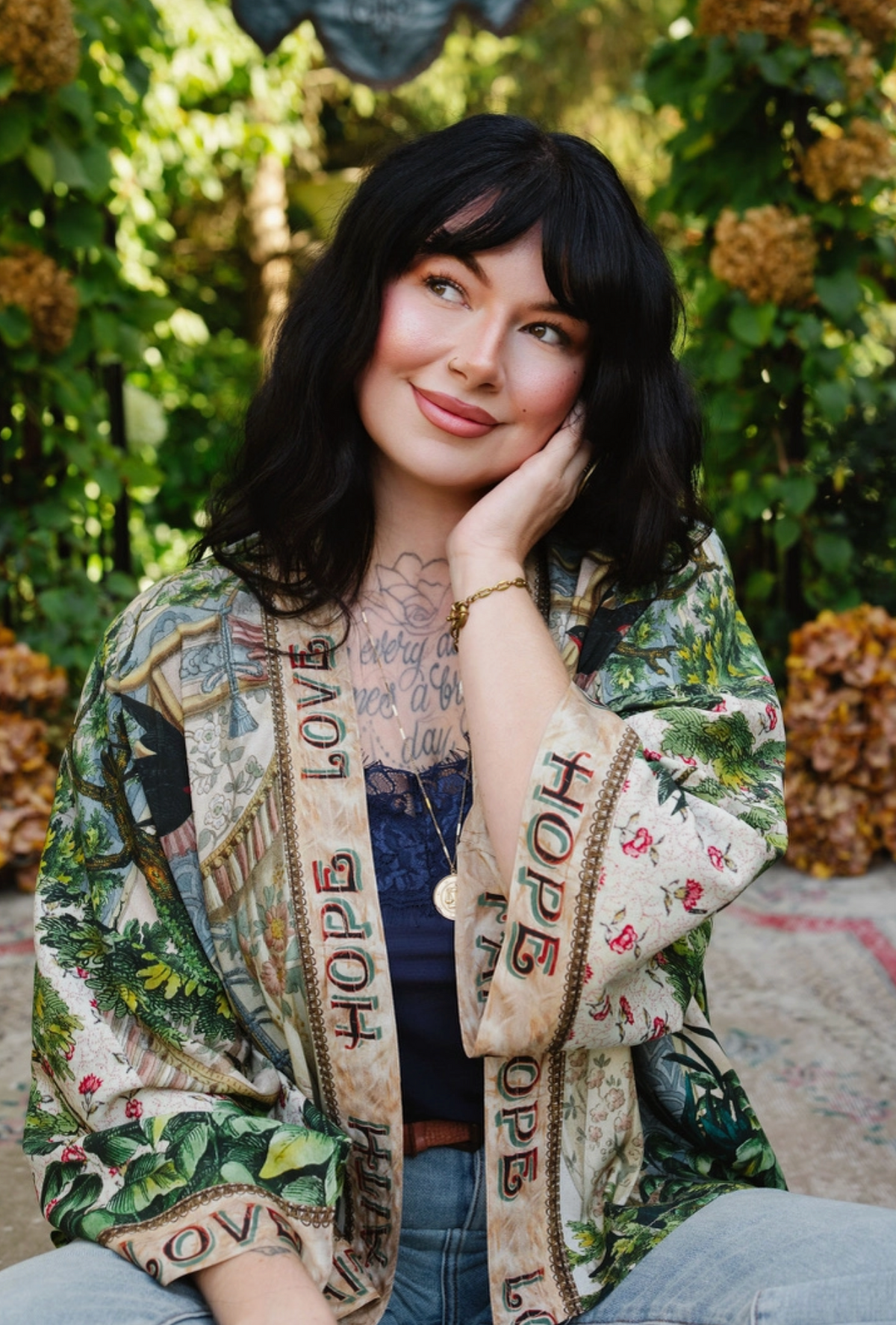  Seated model wearing Book of Love cropped kimono with jeans, showing floral sleeves and Faith Hope Love trim | Bliss by Cori