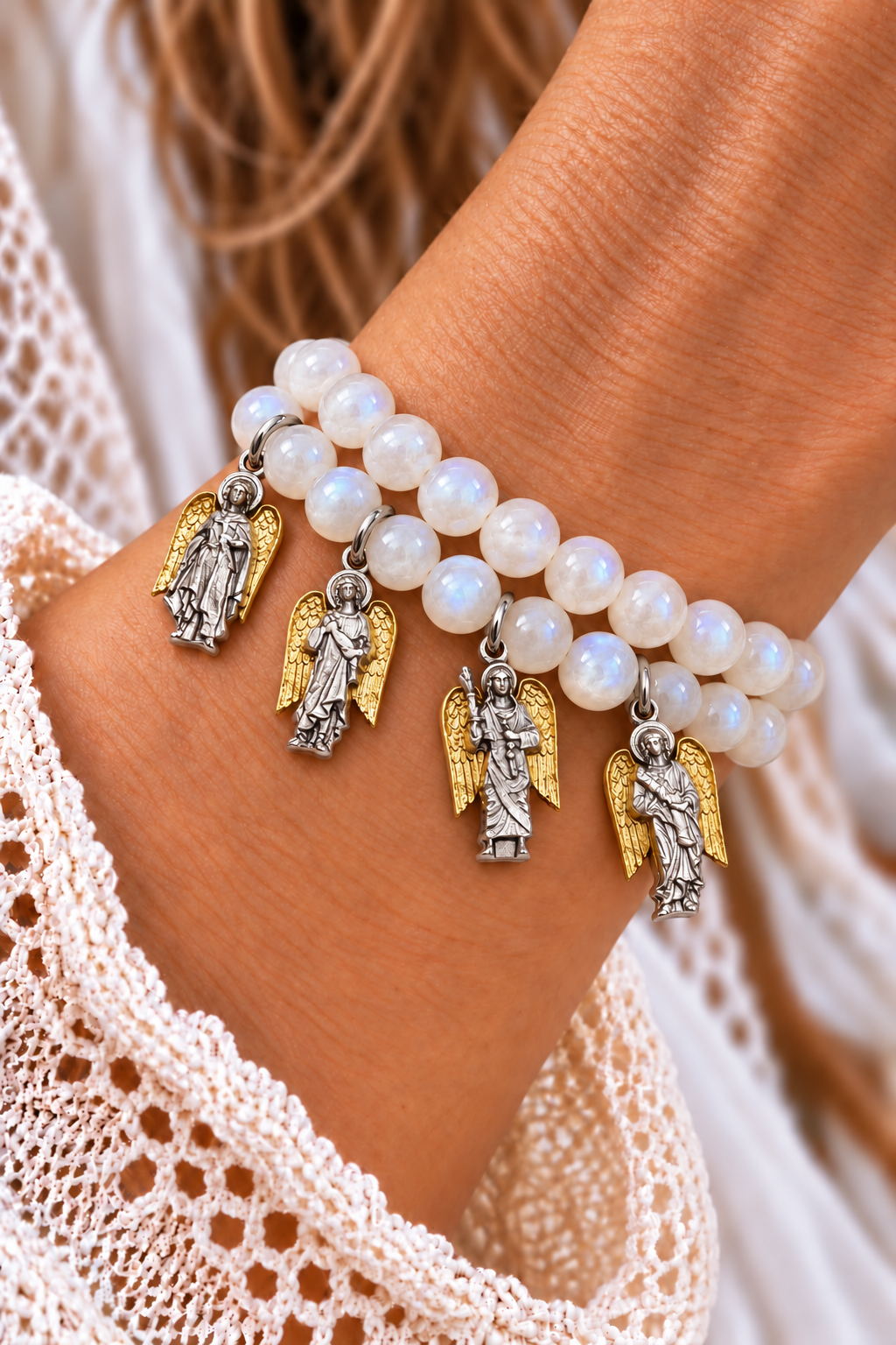 Two white moonstone bracelets with four silver-tone archangel charms and gold-tone wings worn on a wrist | Bliss by Cori