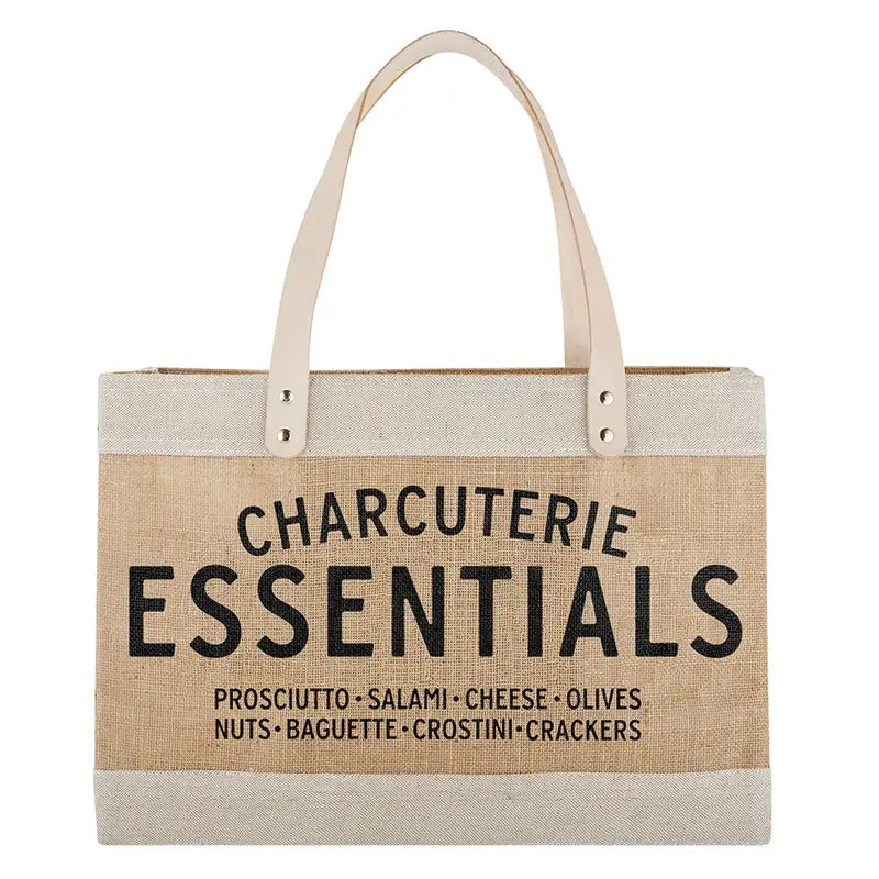 Large natural jute market tote with cream leather handles and black Charcuterie Essentials text listing prosciutto salami cheese olives nuts baguette crostini and crackers on white background – Bliss by Cori
