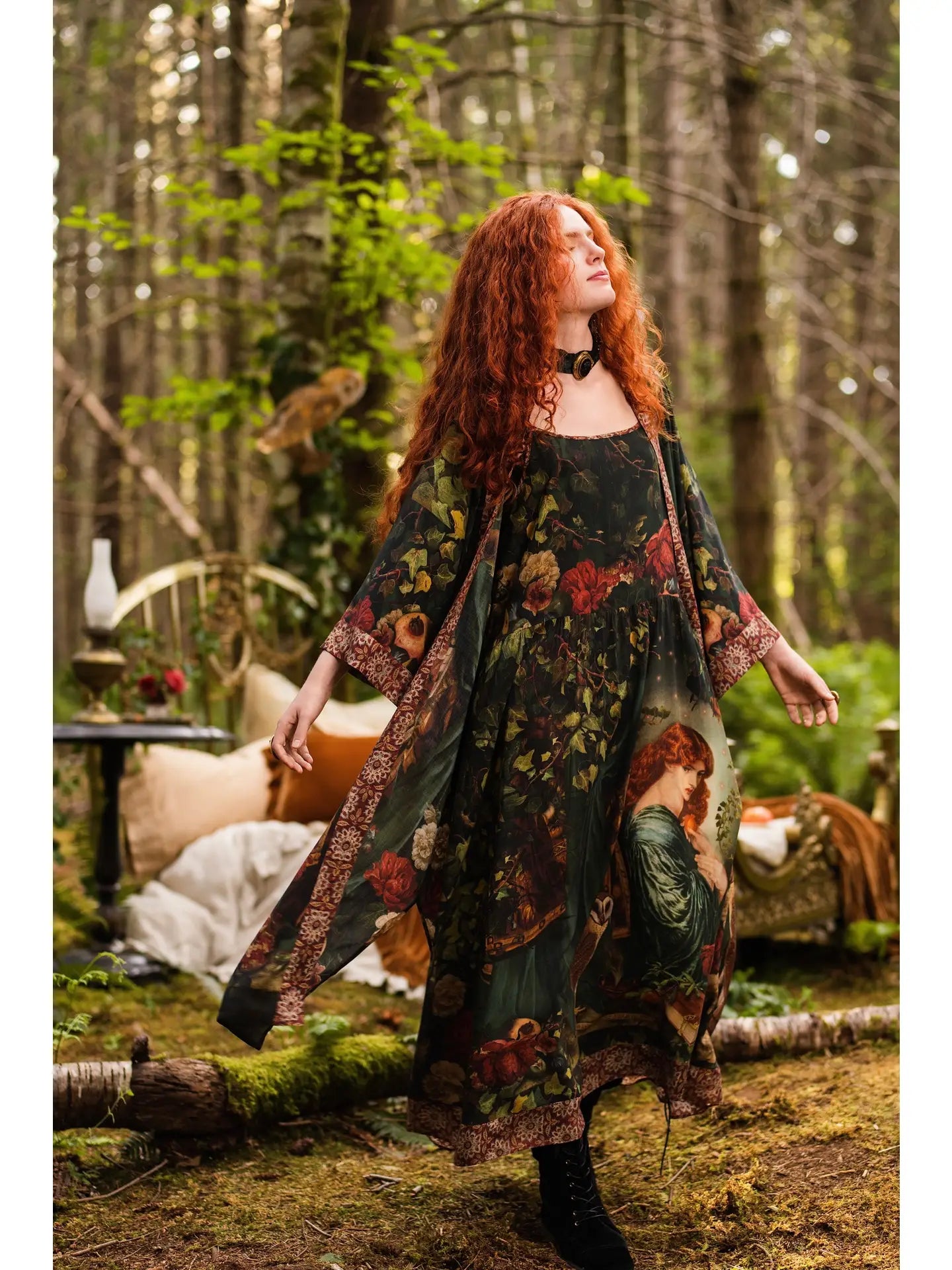 Back view of red-haired model in sunlit forest wearing Solstice Bohéme Maxi Slip Dress, Rossetti Proserpine portrait print cascading to tapestry hem, antique writing desk with candle in background — Bliss by Cori