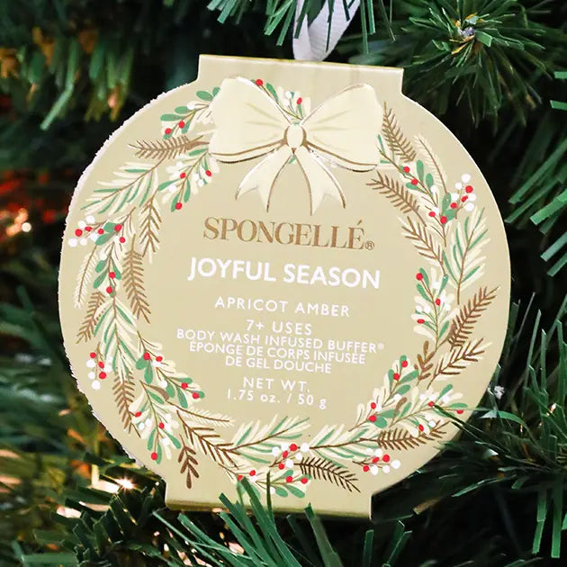 Spongellé Joyful Season Apricot Amber body buffer ornament in gold holiday wreath packaging hanging on Christmas tree — Bliss by Cori Boutique