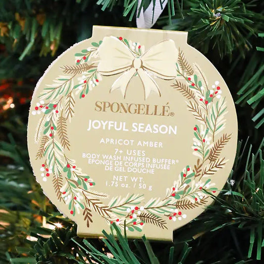Spongellé Joyful Season Apricot Amber body buffer ornament in gold holiday wreath packaging hanging on Christmas tree — Bliss by Cori Boutique