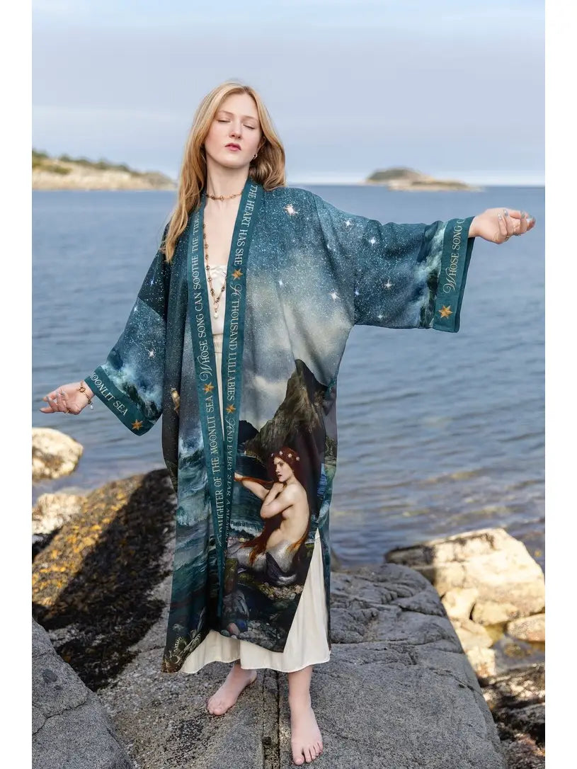 Model holding out the wide sleeves of the Siren full-length duster beside the sea | Bliss by Cori