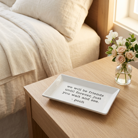White ceramic tray with a friendship quote signed Pooh on a wooden bedside table beside flowers and cream bedding | Bliss by Cori
